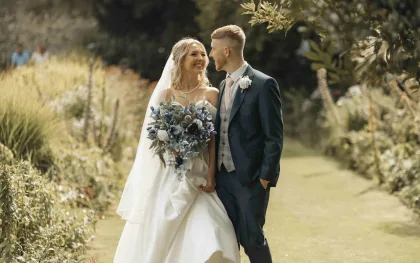 Couple de mariés se promenant dans un jardin, bouquet à la main