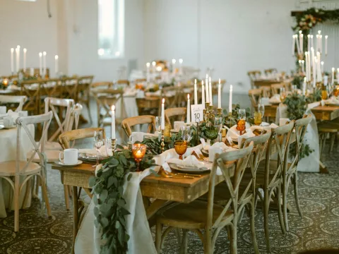 Salle de réception de mariage : longues tables en bois dressées avec bougies et feuillages